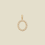 A gold initial 'O' charm featuring small clear round-cut stones, set against a solid light beige background.