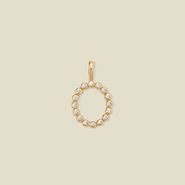 A gold initial 'O' charm featuring small clear round-cut stones, set against a solid light beige background.