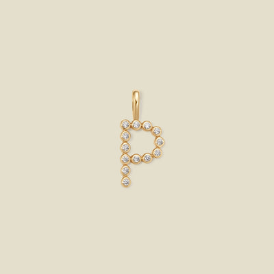 A gold letter 'P' pendant charm embellished with small clear round gemstones, centered on a solid light beige background.
