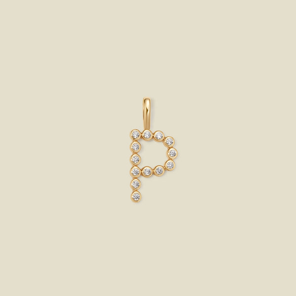 A gold letter 'P' pendant charm embellished with small clear round gemstones, centered on a solid light beige background.