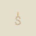 A gold letter 'S' pendant charm embellished with small clear round gemstones, centered on a solid light beige background.