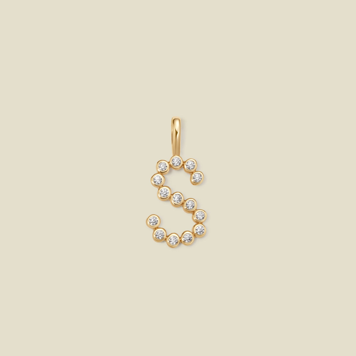 A gold letter 'S' pendant charm embellished with small clear round gemstones, centered on a solid light beige background.