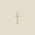A gold initial 'T' charm comprised of clear round bezel-set gemstones, set against a solid beige background.