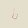 A gold initial 'U' charm made up of small round bezel-set clear stones, set against a solid beige background.