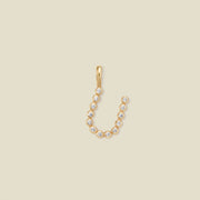 A gold initial 'U' charm made up of small round bezel-set clear stones, set against a solid beige background.