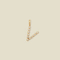 A gold initial pendant charm shaped like the letter 'V', adorned with small clear round gemstones, shown on a solid light beige background.