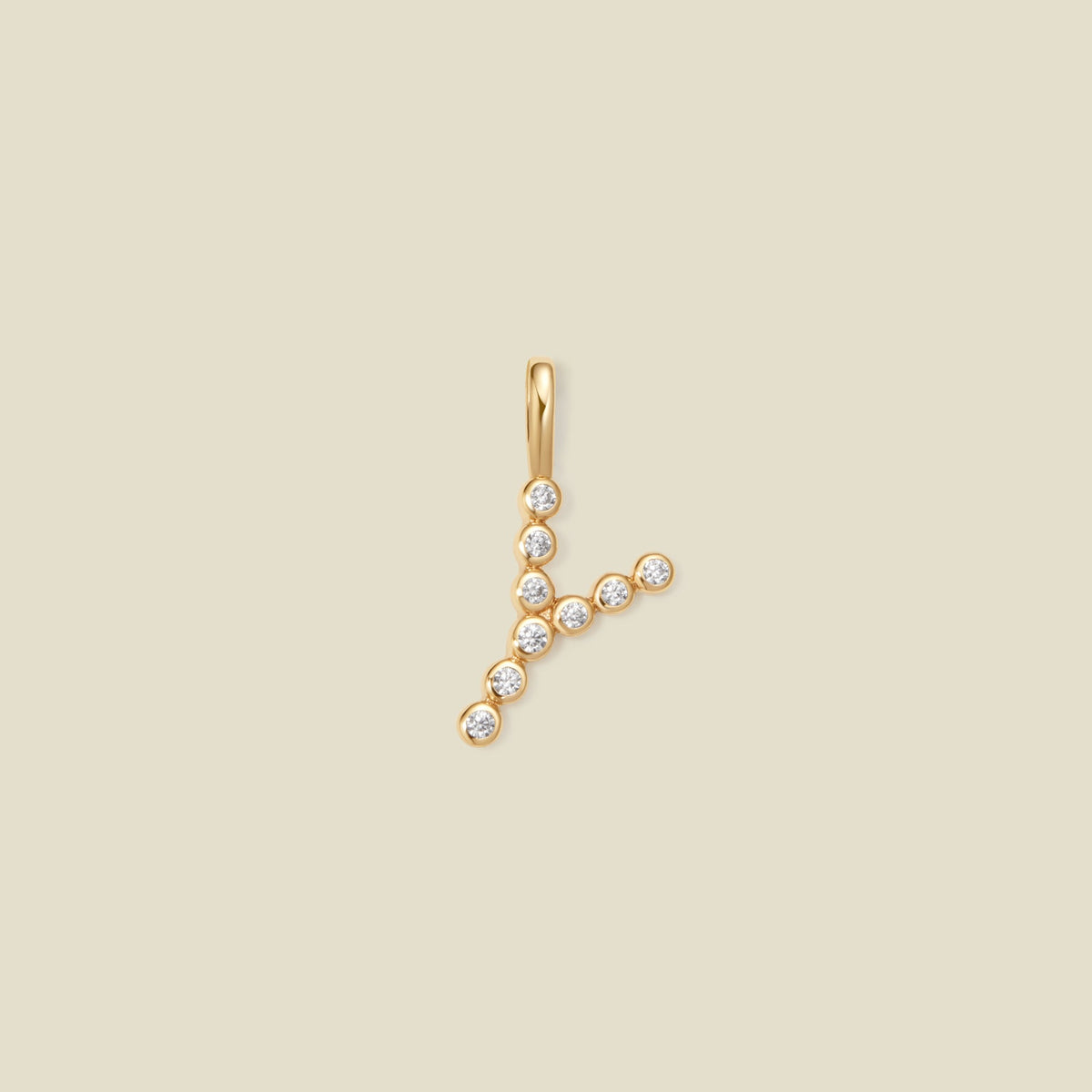 A gold initial pendant 'Y' charm, adorned with small clear round-cut gemstones, set against a solid light beige background.