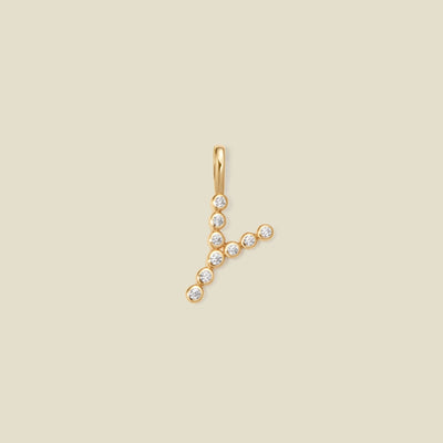 A gold initial pendant 'Y' charm, adorned with small clear round-cut gemstones, set against a solid light beige background.