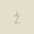A gold initial 'Z' charm made up of small round bezel-set clear gemstones, set against a solid beige background.