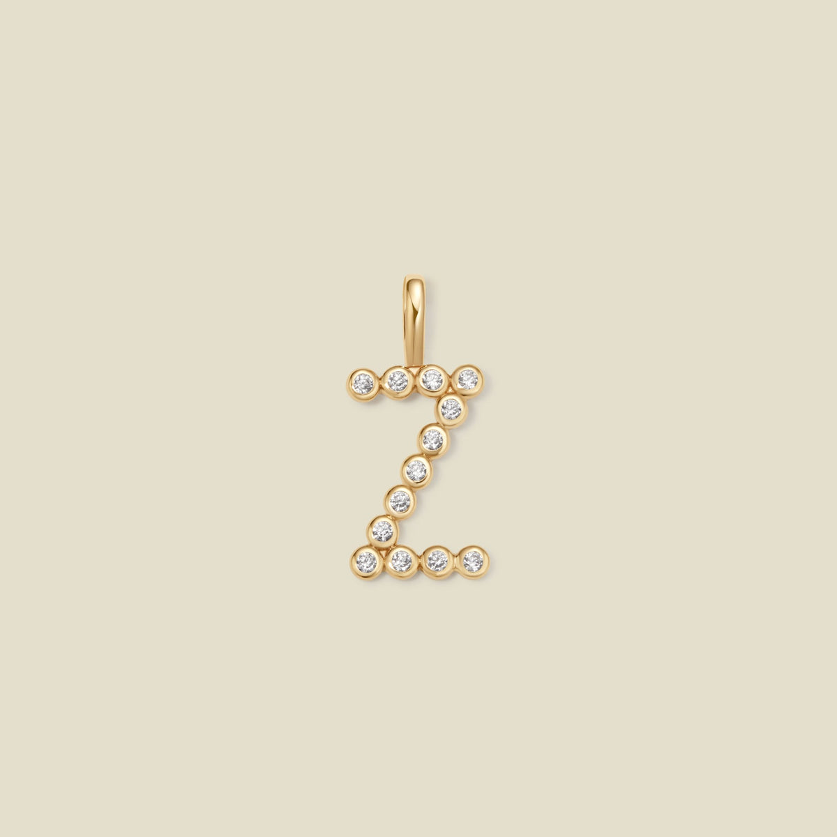 A gold initial 'Z' charm made up of small round bezel-set clear gemstones, set against a solid beige background.