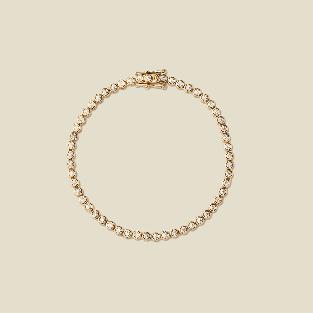 A gold tennis bracelet with clear round-cut gemstones, arranged in a circular shape on a solid beige background.