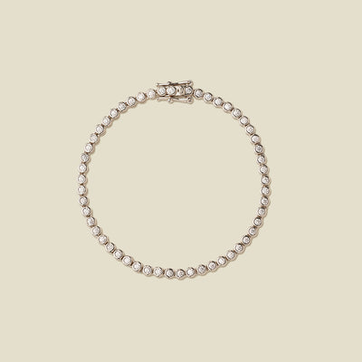 A silver tennis bracelet with clear round-cut gemstones, arranged in a circular shape on a solid beige background.