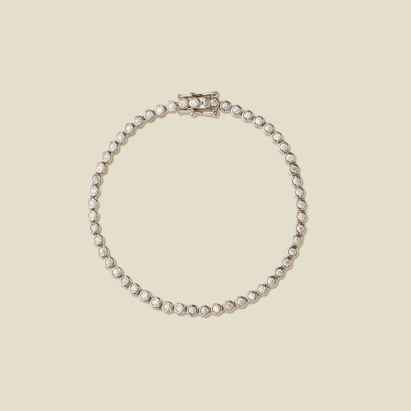 A silver tennis bracelet with clear round-cut gemstones, arranged in a circular shape on a solid beige background.