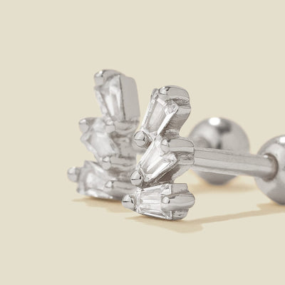 A pair of silver stud earrings with baguette-cut clear stones, shown on a solid light beige background.