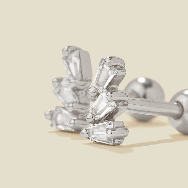 A pair of silver stud earrings with baguette-cut clear stones, shown on a solid light beige background.