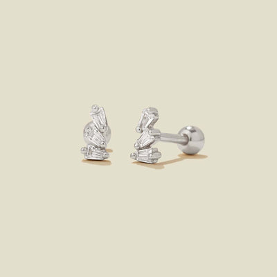 A pair of silver stud earrings with baguette-cut clear stones, shown on a solid light beige background.