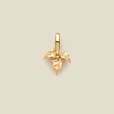 A polished gold holly leaf pendant charm with a hanging loop, centered on a solid light beige background.