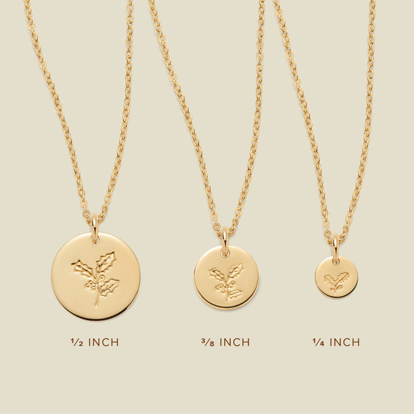 A size comparison chart with three gold pendant necklaces, each with a different size of flat round disc charm in the measurements '1/2 INCH', '3/8 INCH', and '1/4 INCH'. Each of the necklaces is engraved with a holly floral design and shown on a solid light beige background.