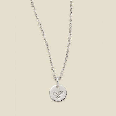A silver chain necklace with a round silver disc pendant engraved with a holly leaf design, shown against a solid light beige background.