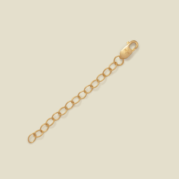 A gold-toned lobster clasp connected to a short chain of oval links, photographed on a plain warm beige background.