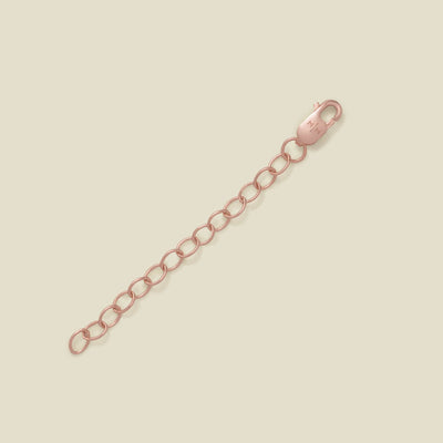 A rose gold lobster clasp connected to a short chain of oval links, photographed on a plain warm beige background.