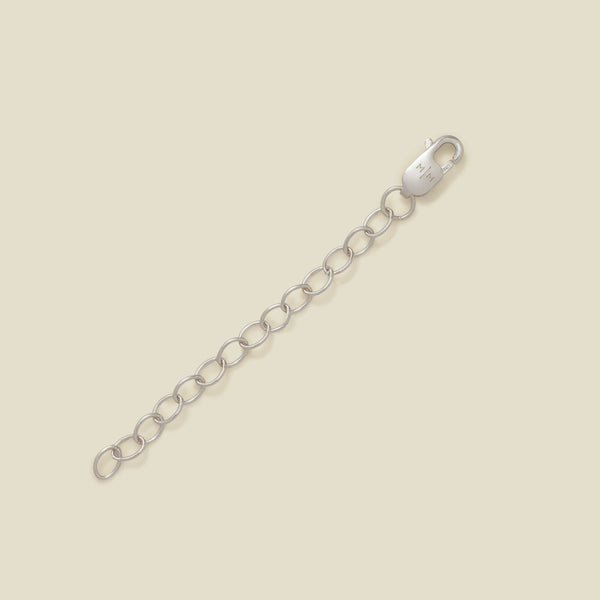 A silver lobster clasp connected to a short chain of oval links, photographed on a plain warm beige background.