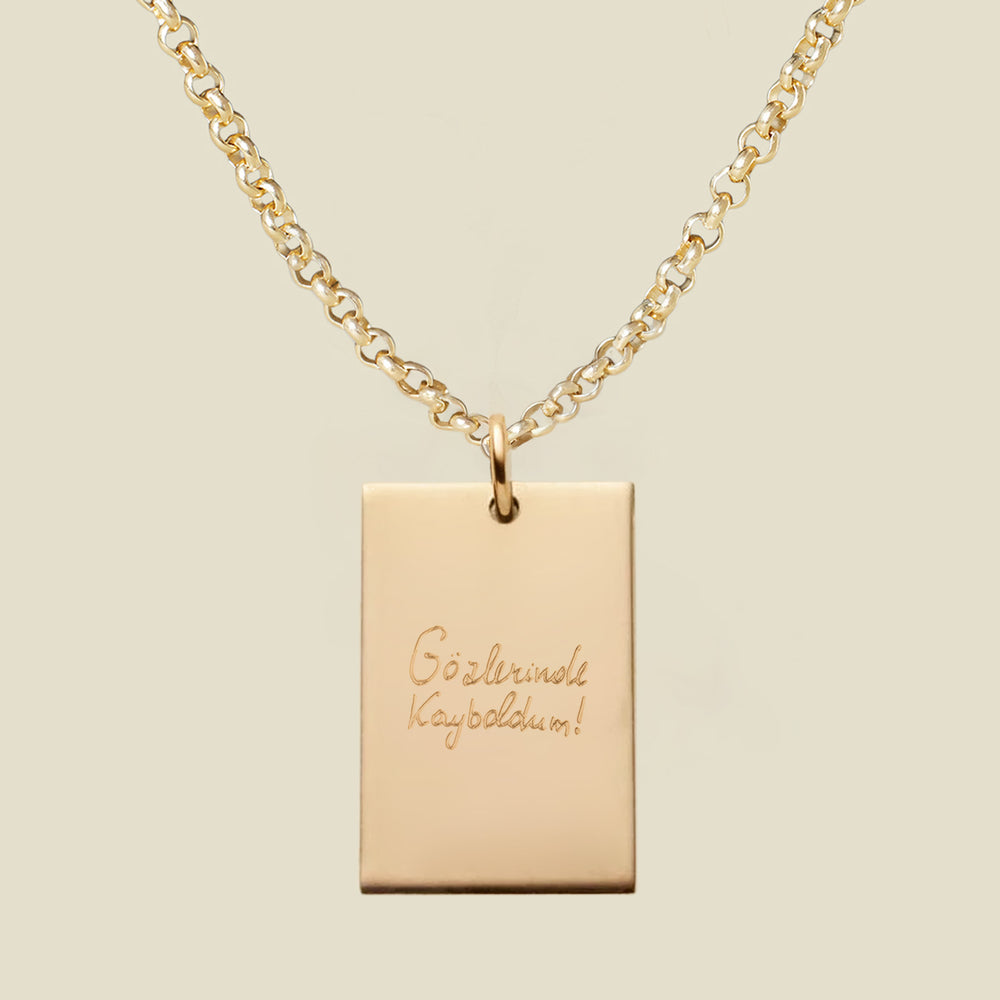 Gold necklace with a rectangular engraved pendant featuring handwritten text on a beige background
