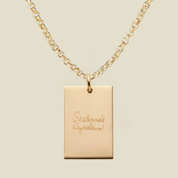 Gold necklace with a rectangular engraved pendant featuring handwritten text on a beige background