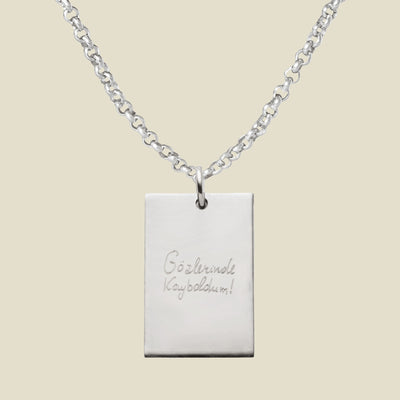 Silver necklace with a rectangular engraved pendant, featuring handwritten text on a beige background