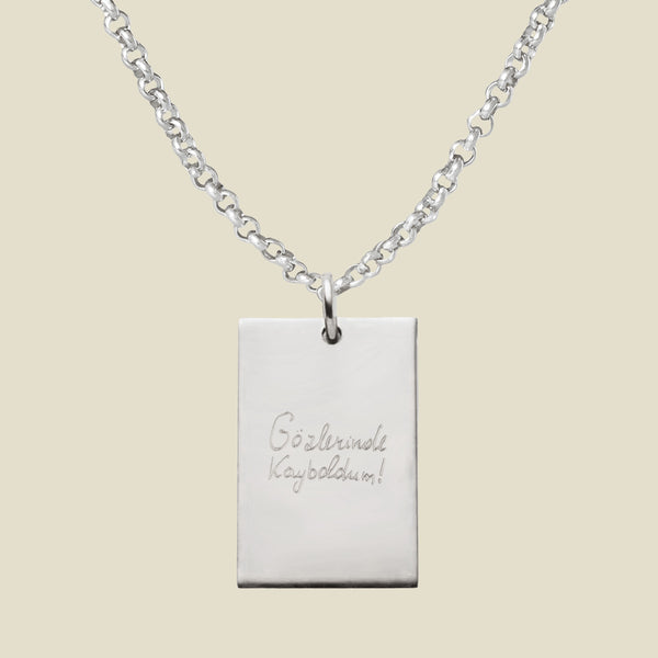 Silver necklace with a rectangular engraved pendant, featuring handwritten text on a beige background