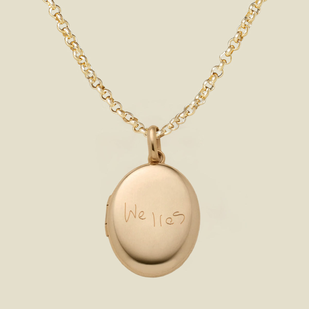 A gold locket necklace with an oval pendant engraved with the name 'Welles', shown on a light beige background.
