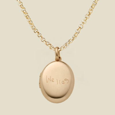 A gold locket necklace with an oval pendant engraved with the name 'Welles', shown on a light beige background.