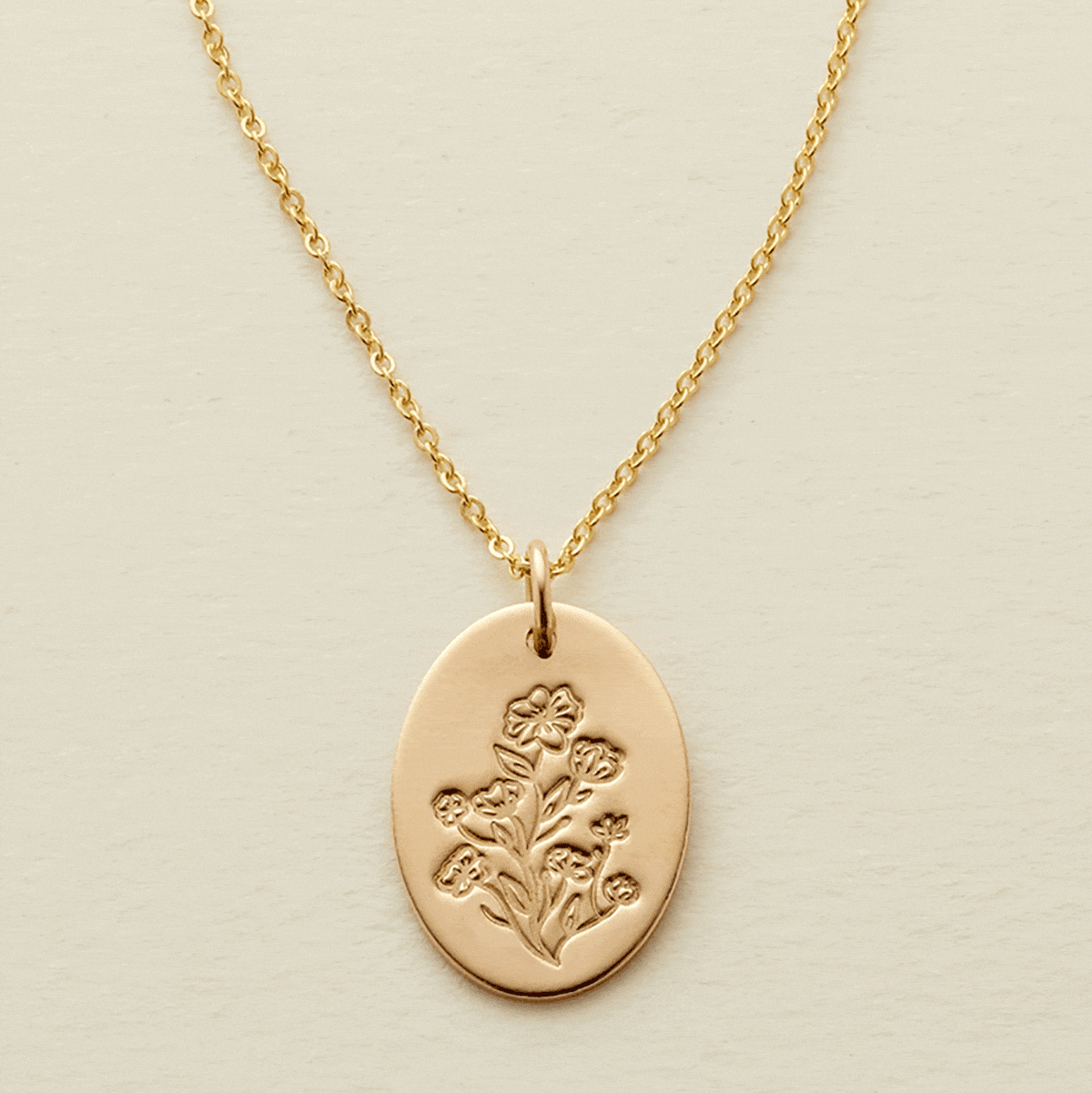 A gif of a delicate gold pendant chain necklace with a flat oval disc charm, showcasing an engraved floral pattern with different numbers of flowers being added and removed from the disc.