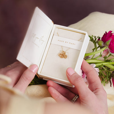 A cream colored jewelry box sitting open holding a gold pendant necklace with three small flower charms.