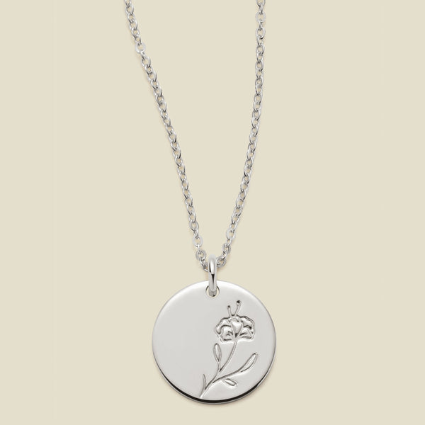 A silver chain necklace with a round silver disc pendant featuring an engraved violet flower design, displayed against a solid light beige background.