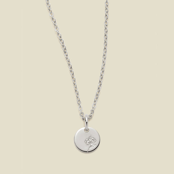 A silver chain necklace with a round silver disc pendant featuring an engraved violet flower design, displayed against a solid light beige background.