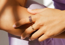 A close up lifestyle shot of a hand wearing multiple stacked gold rings.