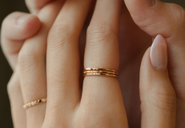 Close-up of fingers wearing gold rings on a neutral background