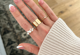 A hand wearing three gold rings, one cocktail style ring with multiple pearls in different sizes, a gold cigar band ring, and a dainty gold ring with a singular pearl.