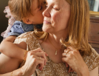 A woman being embraced from behind by a child around the shoulders.
