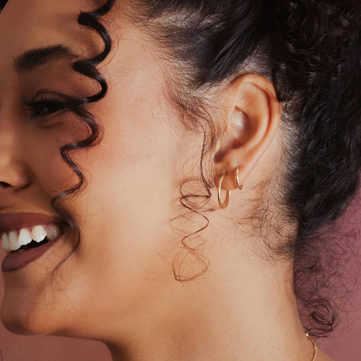 Close-up of a woman's ear with two thin gold hoop earrings in different sizes, focusing on the jewelry.
