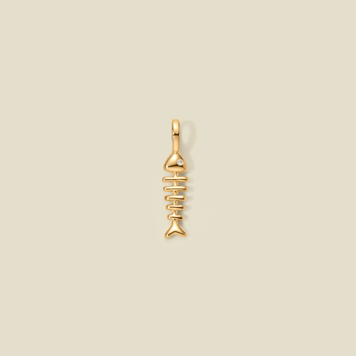 A small gold fish skeleton charm pendant with a polished finish and a top loop, centered on a solid light beige background.