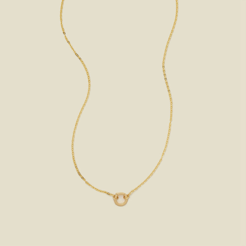 A delicate gold chain necklace with a polished gold round ring in the center, set against a solid beige background.