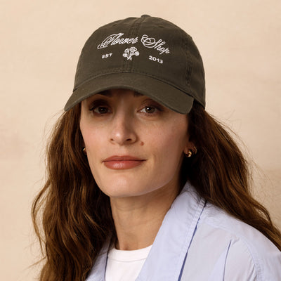Woman wearing a green cap with the text 'Flower Shop' and floral logo on a beige background