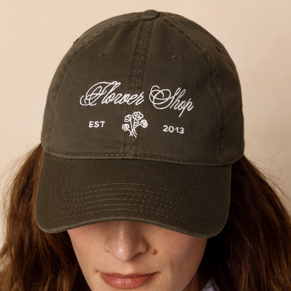 Person wearing a dark green cap with 'Flower Shop' text and logo on a beige background