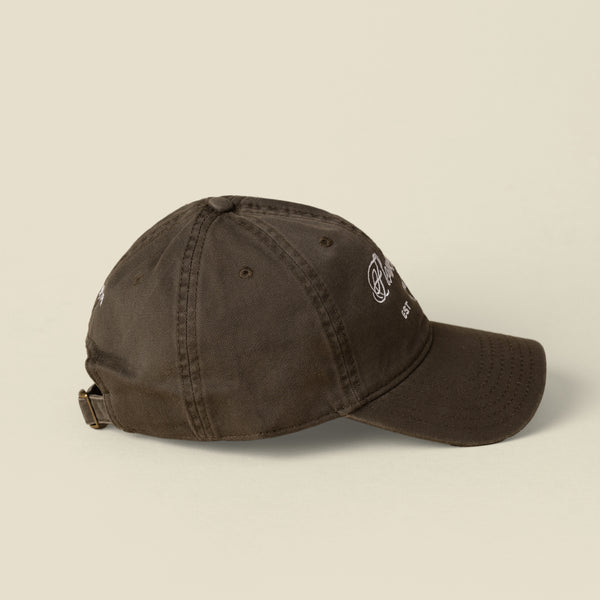 A dark green cotton baseball hat shown from the side, set on a solid beige background.