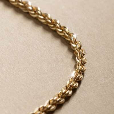 Close-up of a gold chain with a rope texture on a beige background