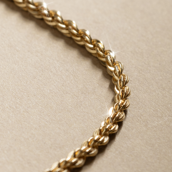 Close-up of a gold chain with a rope texture on a beige background