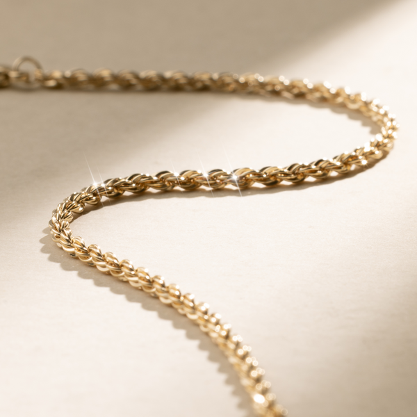 A textured gold chain bracelet, set against a neutral background with natural shadows.