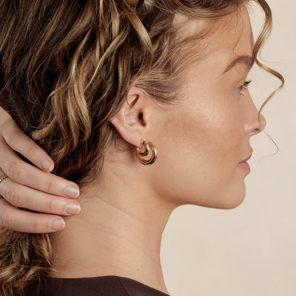 A close-up of a woman's ear wearing two pairs of polished gold hoop earrings in different sizes.